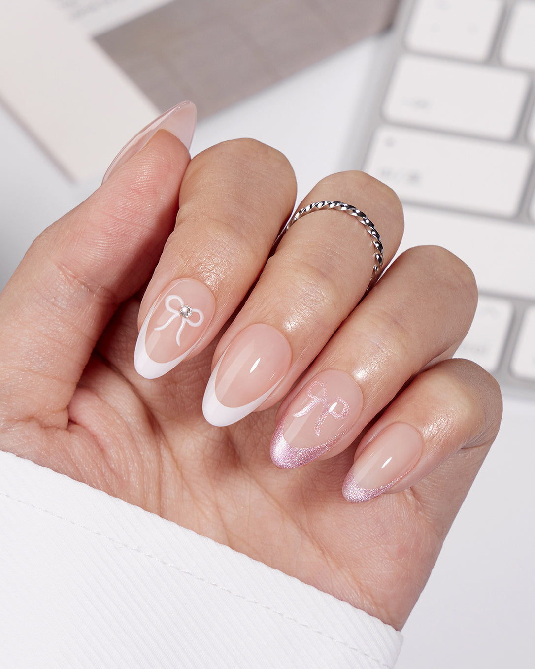 Lover's Note pink French tip press-on nails styled on hands with bow accents creating a feminine coquette manicure look for romantic occasions