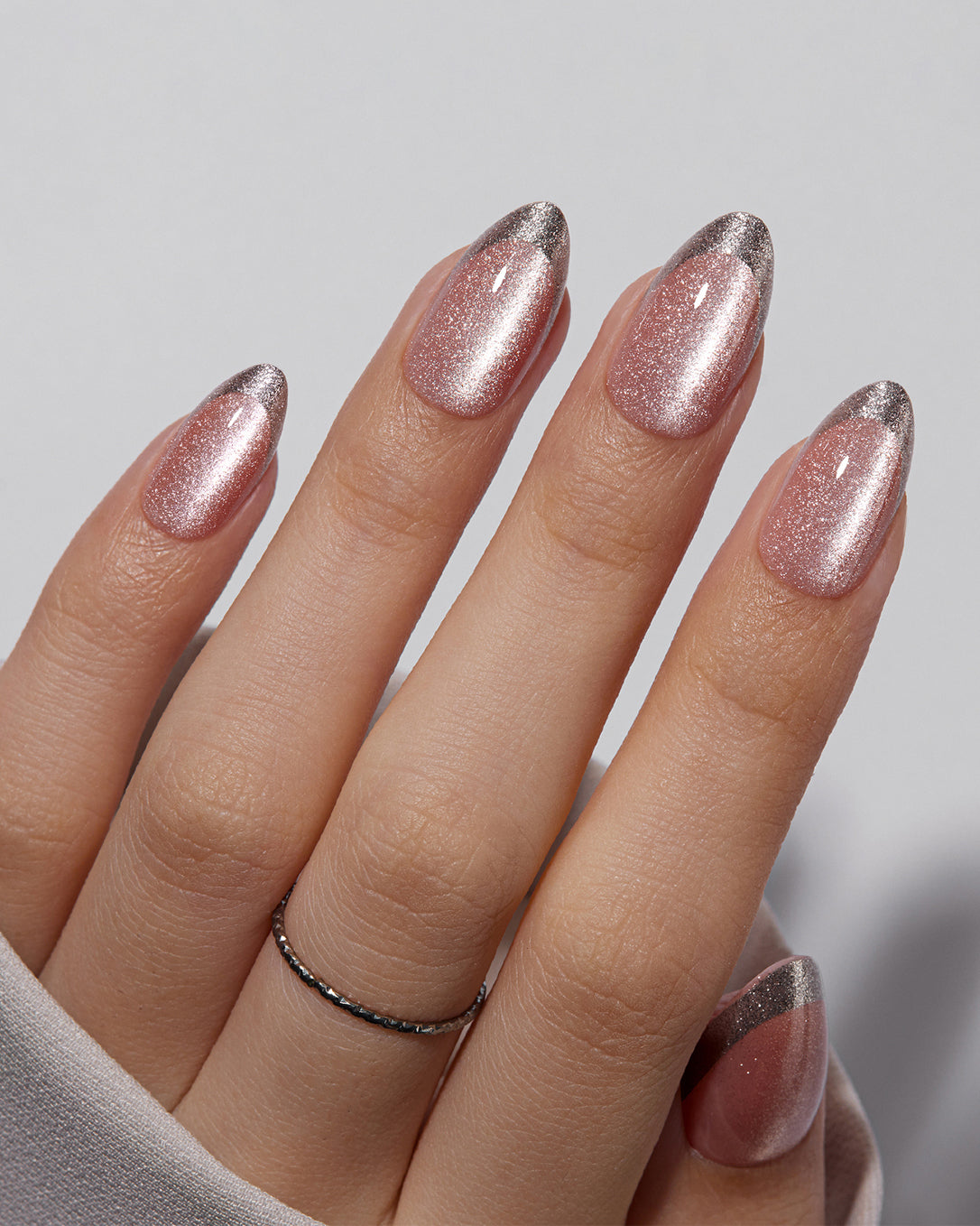 Close-up of pink shimmer almond press-on nails with metallic French tips and smooth UV gel shine