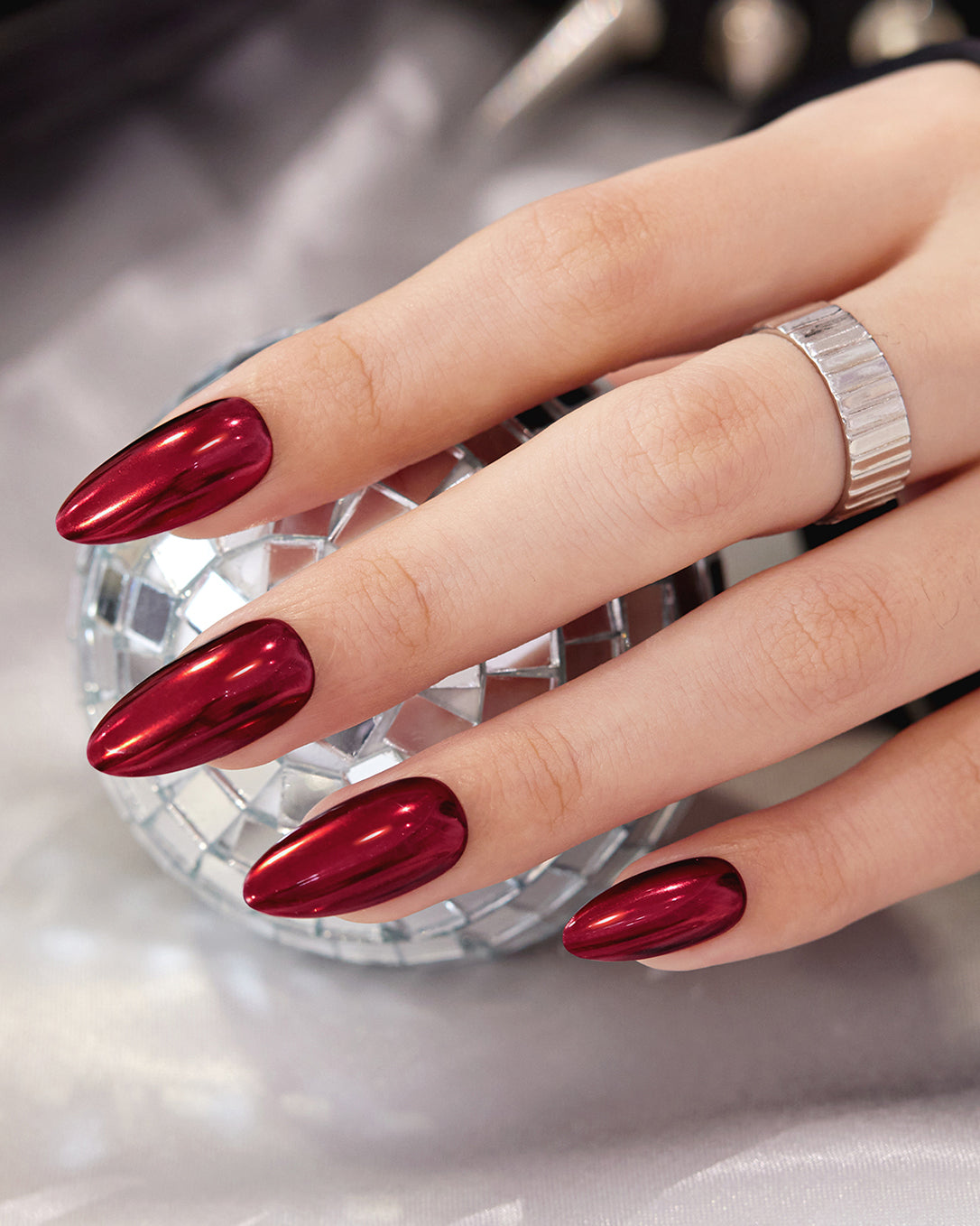 Model wearing VSALON Bourgogne Glide almond press-on nails with a luxurious metallic ruby red manicure.